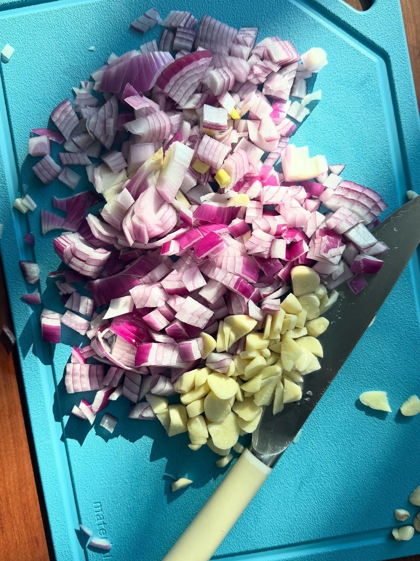 Chopped red onions and sliced garlic on a blue cutting board with a knife.