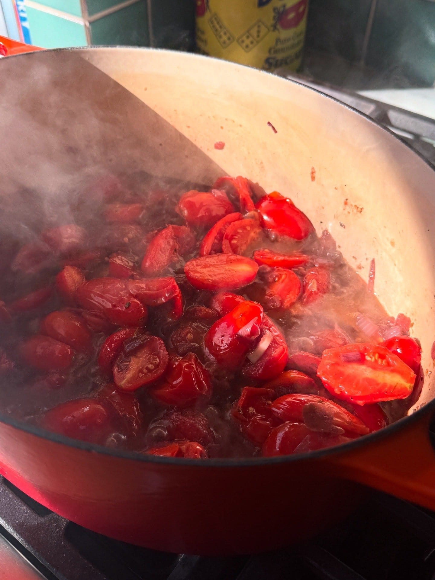 Chopped tomatoes simmering in a red enameled cast iron pot on a stovetop with visible steam rising.