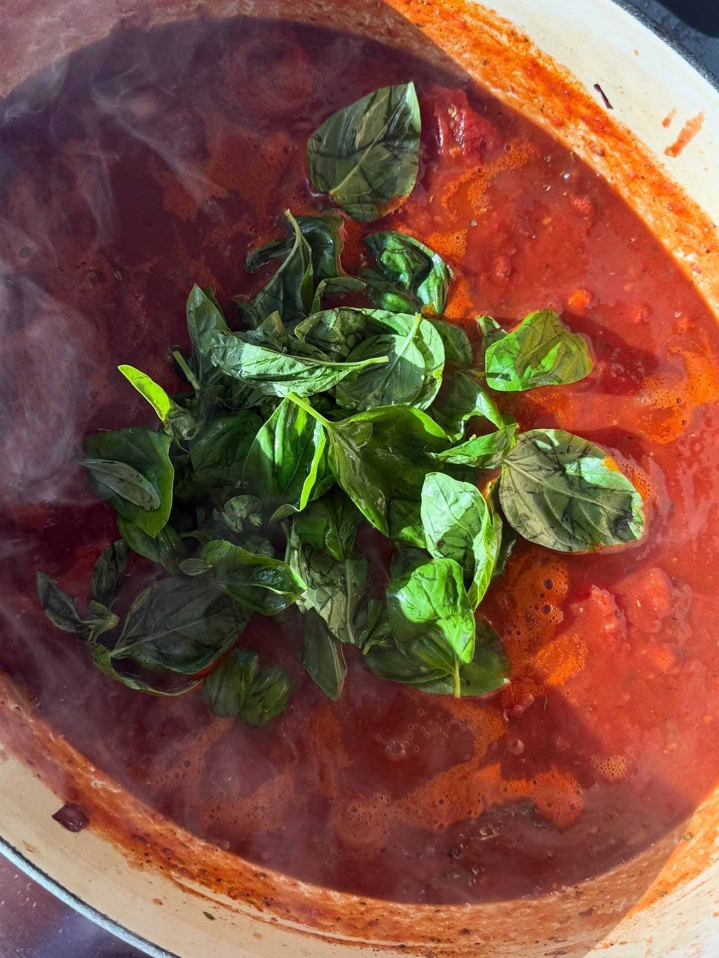 A pot of tomato sauce simmering with fresh basil leaves on top.