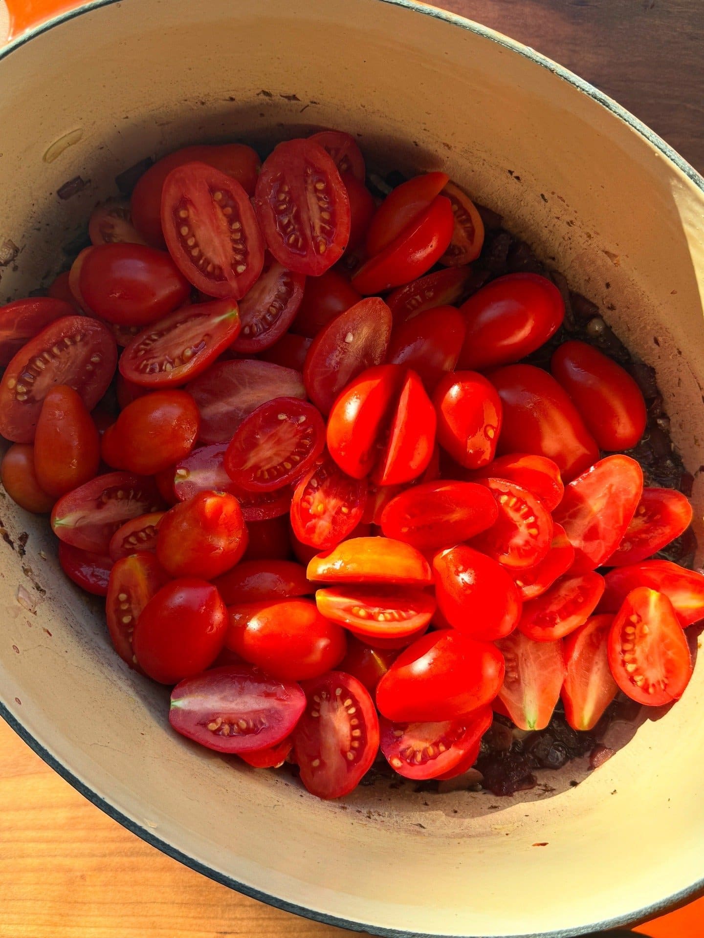 A large pot filled with halved cherry tomatoes on top of chopped vegetables, ready for cooking, lit by natural sunlight.