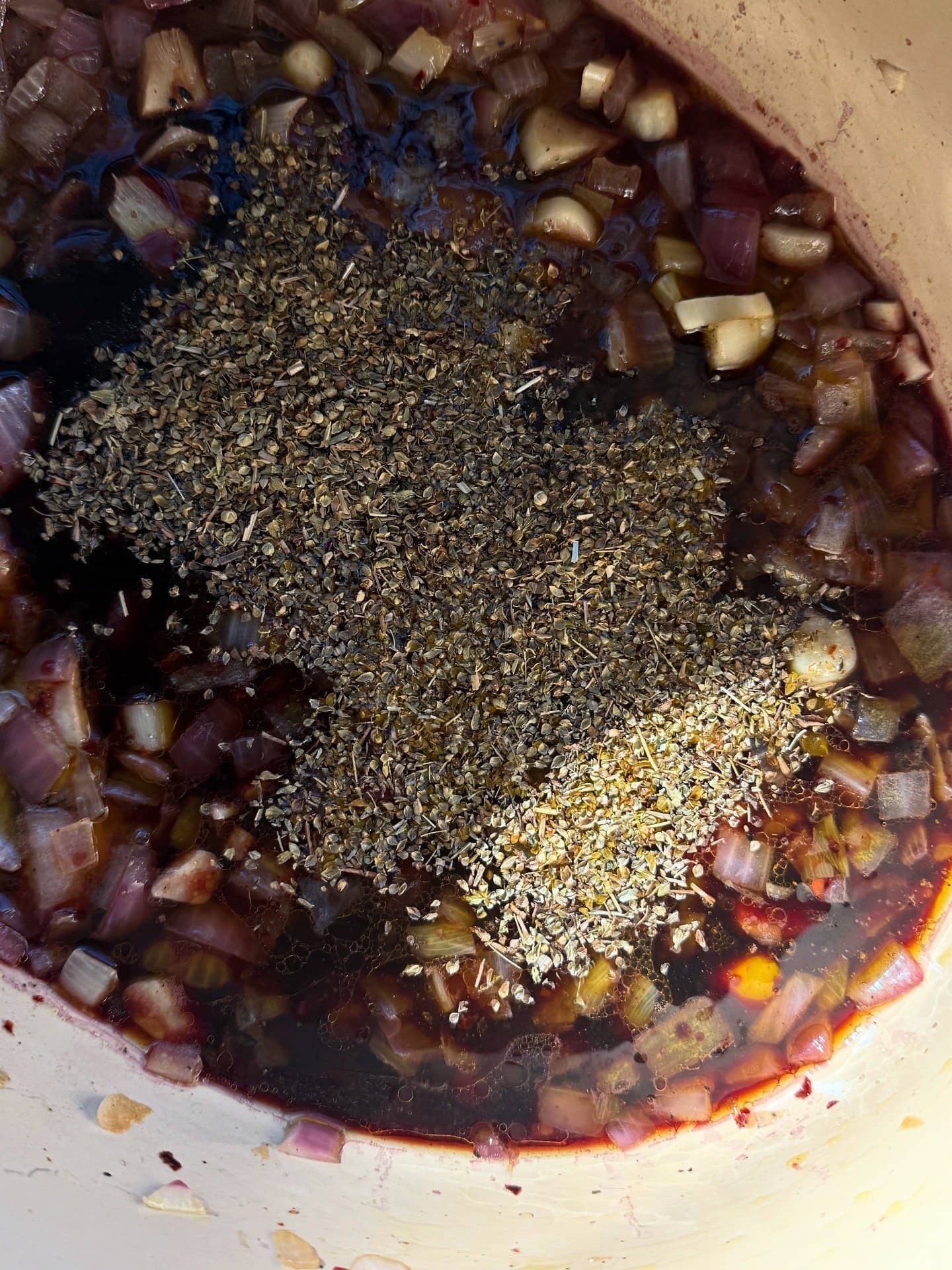 Chopped onions, garlic, dried herbs, and dark liquid simmering in a pot.