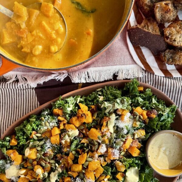 A pot of squash soup, a plate of toasted bread, and a kale salad topped with roasted squash, seeds, and dressing.
