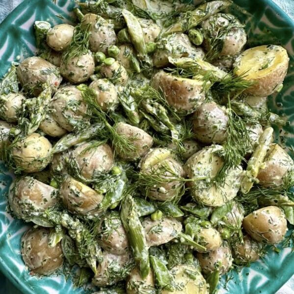 A green plate filled with baby potatoes, asparagus, peas, and fresh herbs in a creamy dressing.
